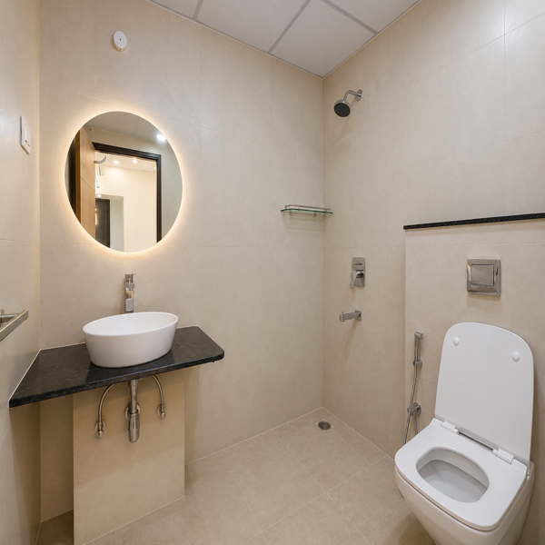 Modern bathroom, luxury bathroom, contemporary bathroom, spacious bathroom, apartment bathroom, elegant bathroom, stylish bathroom, bathroom interior, modern washroom, residential bathroom, wall mounted basin, countertop wash basin, white vessel sink, black granite countertop, illuminated mirror, round mirror, LED mirror, vanity area, bathroom vanity, wall tiles, beige tiles, neutral color palette, modern shower, wall mounted shower, shower area, bathroom fixtures, toilet seat, western toilet, bidet spray, chrome faucet, bathroom fittings, glass shelf, storage area, clean bathroom, bright bathroom, minimalist design, contemporary decor, glossy tiles, tiled flooring, ceiling panels, false ceiling, recessed lighting, ambient lighting, modern architecture, premium apartment, luxury home, residential interior, neat washroom, functional bathroom, elegant home, modern living, real estate interior.